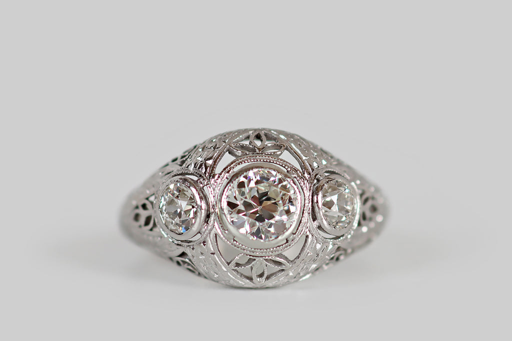 Antique Jewelry Portland, Vintage Jewelry Portland , Antique Engagement Rings | Poor Mouchette | A wonderful, early-Art-Deco-era filigree engagement ring, modeled in platinum, whose gems are a trio of lively old European cut diamonds: a primary .50 carat diamond (I/J, I1), flanked by a pair of .19 carat diamonds (H/I, VS). These charming, hand-cut stones rest in floating bezels, where they are surrounded by crisp, intricate decor elements.