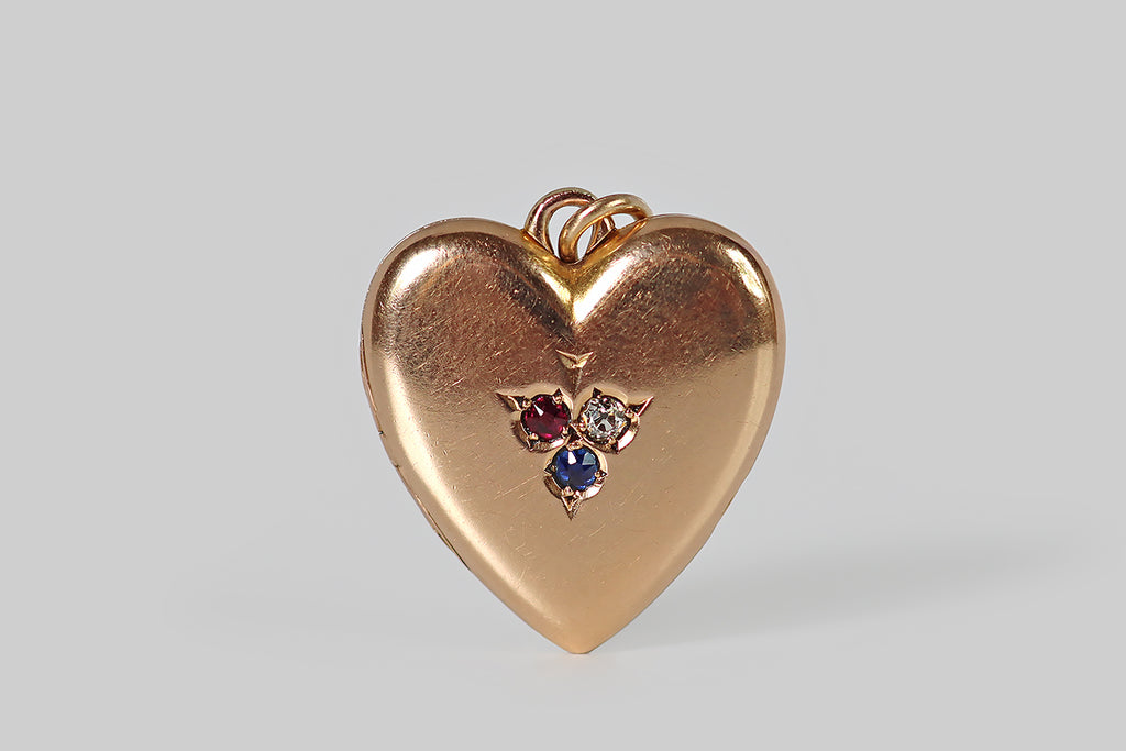 Poor Mouchette | Curated Antique Jewelry, Vintage Jewelry & Engagement Rings | Portland, Oregon | A Victorian-era heart-shaped locket, modeled in 14k rosy yellow gold, whose face is decorated with a beautiful, hand-graved, gem-set trefoil. This stemmed trefoil is inverted, so its central leaf points toward the point of the heart. It is bead-set with three, small old-cut gems— a diamond, a ruby, and a sapphire— to symbolize the French tricolour flag. 