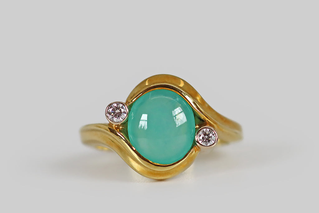 Poor Mouchette | Curated Antique Jewelry, Vintage Jewelry & Engagement Rings | A late vintage ring, modeled in 18k yellow and white gold, whose character is defined by the fluid, satiny, sash-like forms that cradle the ring's central, chrysoprase cabochon. This glowing, oval chrysoprase is held in the modified-bezel these curving yellow-gold forms create. Astride it (to the SE and NW) a pair of sparkling, RBC diamonds