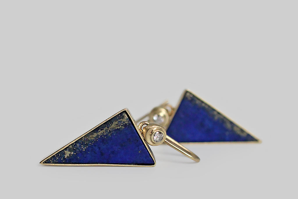 Azure-blue, triangular slabs of lapis lazuli dangle beneath a bright pair of brilliant-cut white diamonds. The diamonds are mounted in an exaggerated bezel, which is circular and subtly organic in form. The lapis triangles are matte finished, and their book-matched edges are figured with a heavy streak of golden pyrite— they're are held in full, open-back bezels, and oriented point-down so they read like arrows, darts, or bolts of lightening.