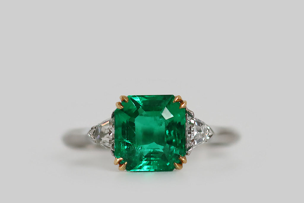 Antique Jewelry Portland, Vintage Jewelry Portland , Antique Engagement Rings | Poor Mouchette | An elegant Art Deco era engagement ring, modeled in platinum and 18k yellow gold, whose primary gem is an especially fine Colombian emerald (approx 1.9 carats). This square, step cut emerald has that most covetable, vivid, deep-bluish-green hue and remarkable transparency— it glows atop the ring's face, where it rests in a yellow gold basket.