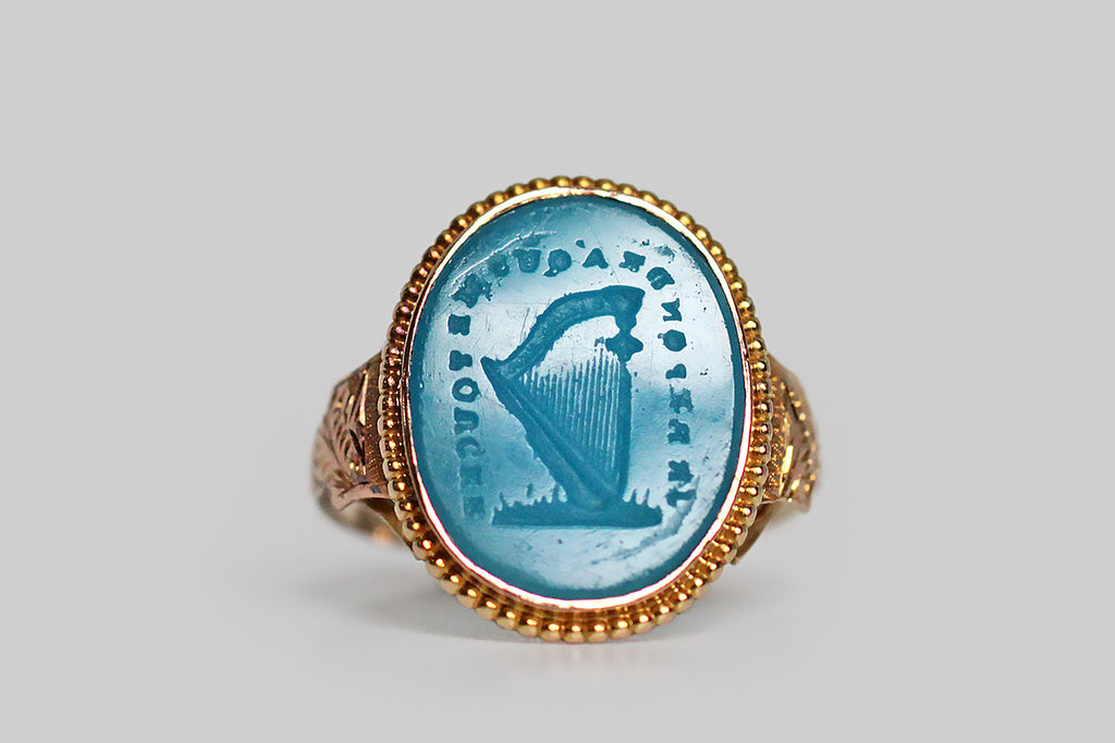 An especially rare and ephemeral Georgian era signet ring, mwhose turquoise glass intaglio seal is carved with an image of a harp, surrounded by the phrase “je reponds á qui me touche:” I respond to every touch. This beautiful old Tassie seal is still partnered with its original high karat gold ring mount. 