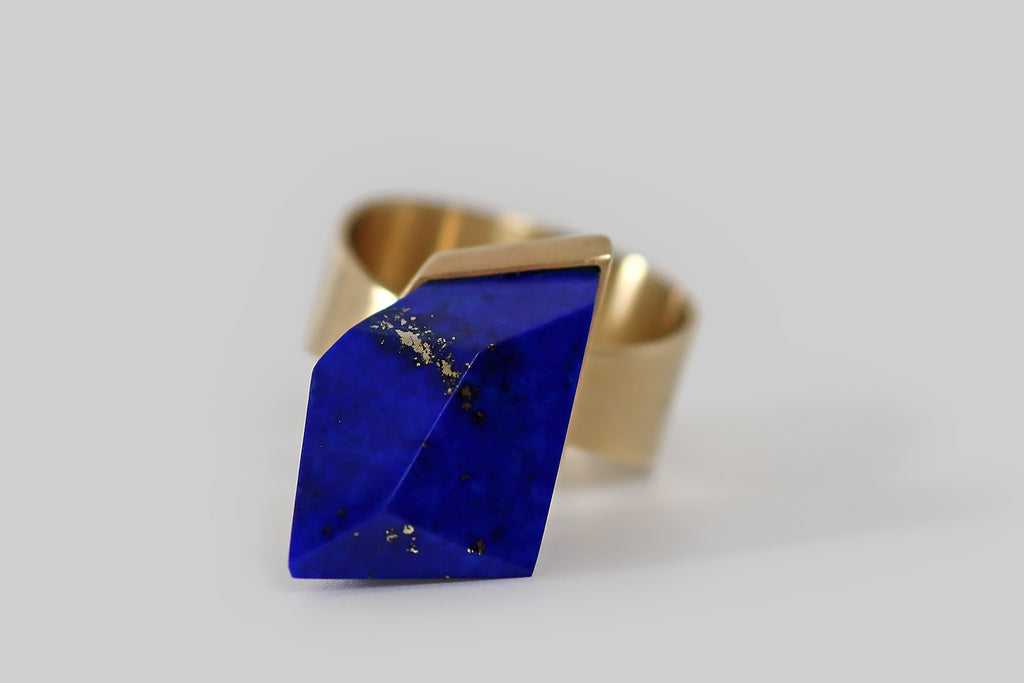 Antique Jewelry Portland, Vintage Jewelry Portland , Antique Engagement Rings | Poor Mouchette | A challenging modernist ring, created by Poor Mouchette, in 14k yellow gold. This ring features an especially vibrant lapis lazuli gem, that is figured with bright gold flecks and splashes of pyrite. This lapis gem is cut with many large, blocky, irregular facets— it is set in a precisely fabricated bezel that floats atop the ring's broad, flat shank. The ring shank is tapered, to widen at the base. 