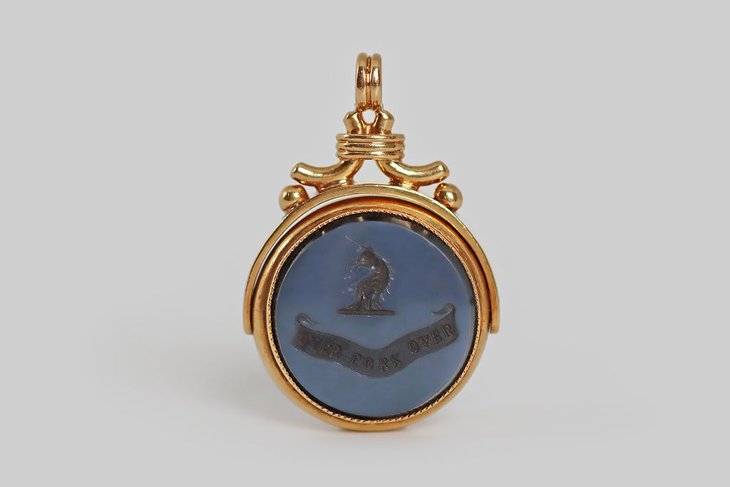 Antique Jewelry Portland, Vintage Jewelry Portland , Antique Engagement Rings | Poor Mouchette | A wonderful, large, Victorian-era fob, modeled in 15k yellow gold and set with an intaglio carved, layered (blue) agate gem. This fine, hand-carved, wax seal is two-sided; it features a unicorn's head on one side, and a monogram (HC) on the other. The unicorn is heroic— shown in profile atop a ribbon base, its beard and mane wave. Below our unicorn's head, a curling banner features the motto "over fork over," 