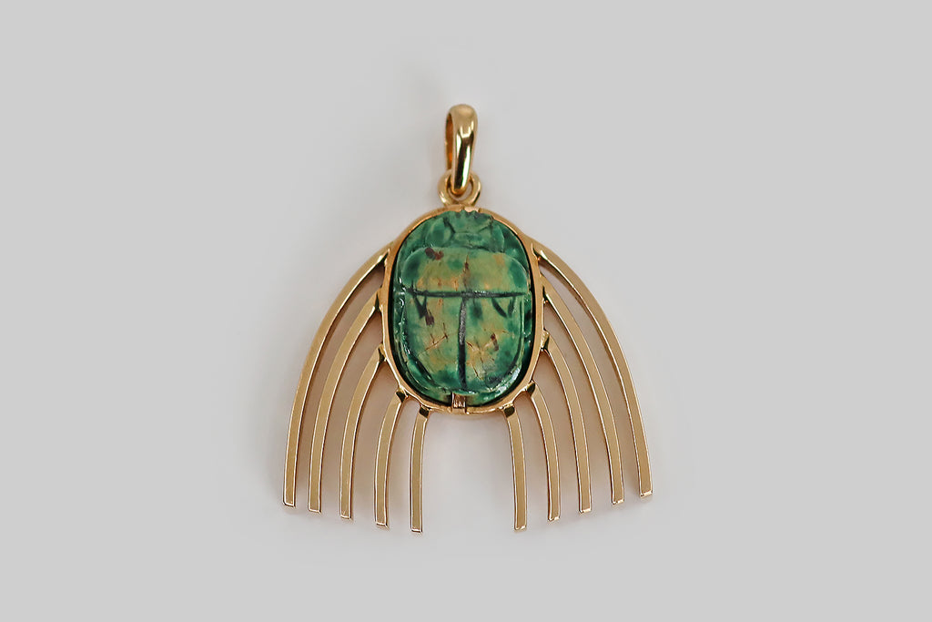 Antique Jewelry Portland, Vintage Jewelry Portland , Antique Engagement Rings | Poor Mouchette | A wonderful, unusual pendant, modeled in rosy 14k yellow gold, featuring a carved faience scarab, decorated with a blue-green glaze. This scarab beetle is set in a low profile bezel; series of heavy arched wires lay astride it, like wings. We love the upward movement implied by the wings here— we see them as swift, rainbow-like (even celestial, intergalactic), and truly cheerful! 