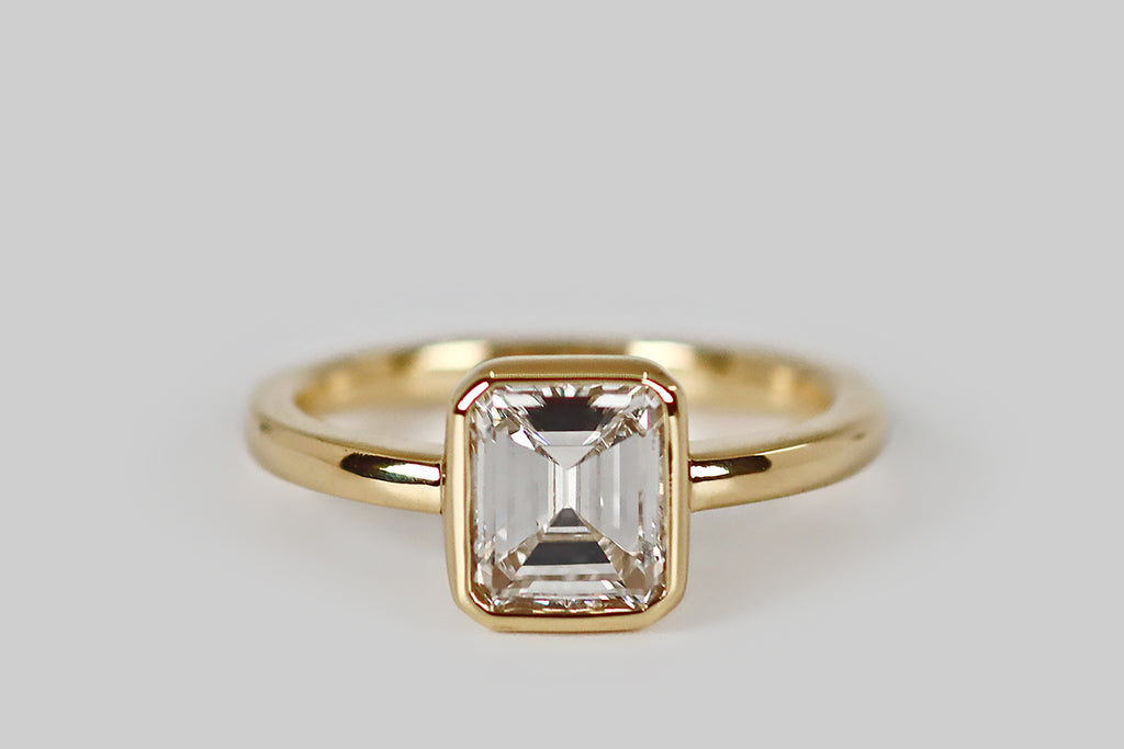 Antique Jewelry Portland, Vintage Jewelry Portland , Antique Engagement Rings | Poor Mouchette | Timeless and refined, an antique, 1.45 carat emerald-cut diamond rests inside a polished, low-profile bezel. This smooth bezel has crisp lines, with soft edges; it connects seamlessly to the ring's substantial, half-round shank. This engagement ring is modern, minimalist, and subtly geometric; its antique diamond is white (I) and very clear (VS1), with an especially large face-up