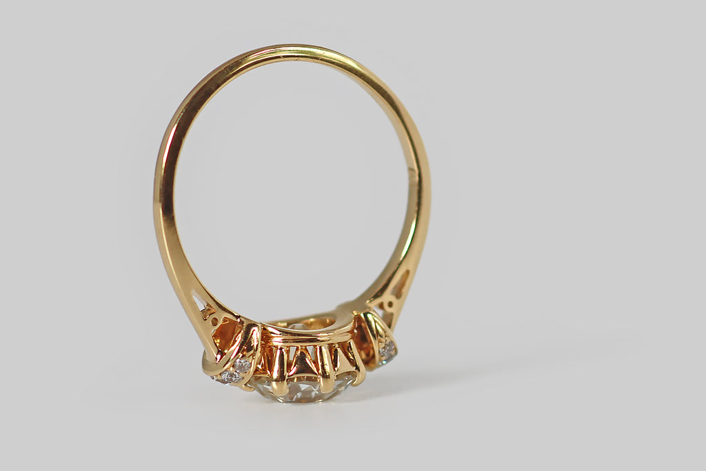 Poor Mouchette | Curated Antique Jewelry, Vintage Jewelry & Engagement Rings | Portland, Oregon | An elegant engagement ring, modeled in 18k yellow gold, whose primary gem is a striking 1.8 carat, old European cut diamond (GIA: L, SI1). This antique diamond is symmetrical and masterfully cut— it is held in eight prongs, atop the ring's crown-like basket, and its open culet reflects repeatedly in the stone's crown facets, creating a striking Kozibe effect!