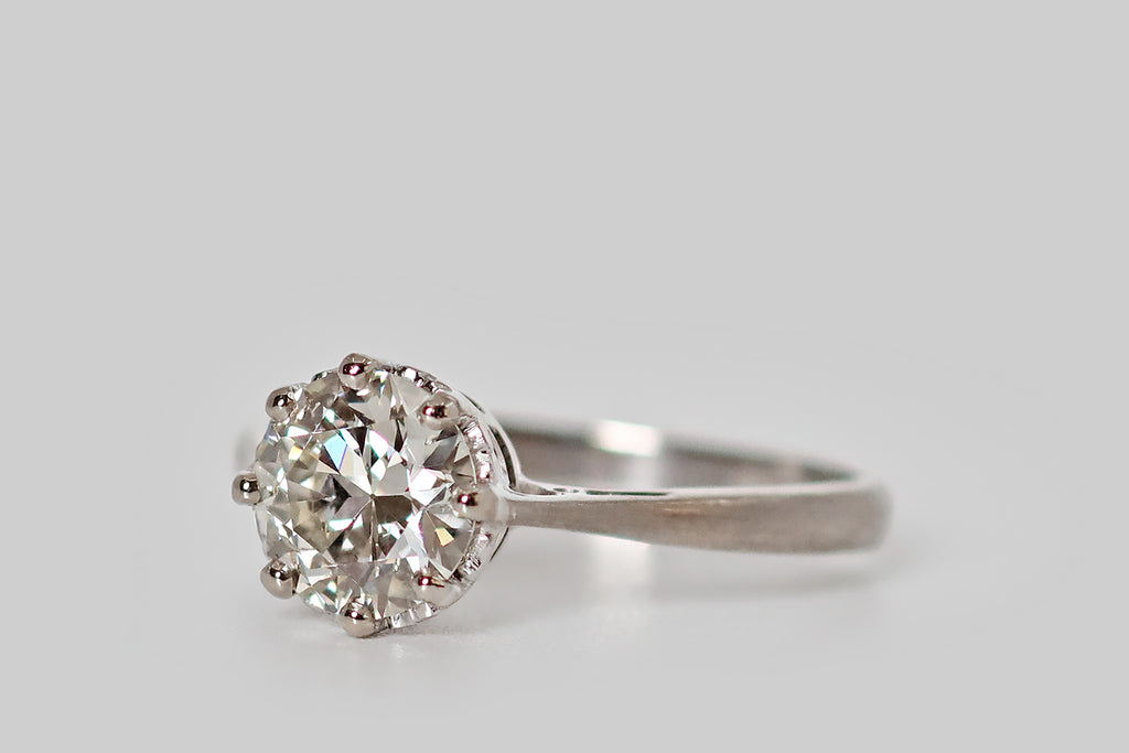 Antique Jewelry Portland, Vintage Jewelry Portland , Antique Engagement Rings | Poor Mouchette | An elegant 1940s engagement ring, modeled in 18k white gold, whose single gem is a vibrant 1.3 carat transitional cut diamond (H, SI1). This wonderful antique diamond sits in a crown-like basket, where it is held in place by eight prongs. The ring's shank is pinched at the shoulders, creating a lovely, delicate-looking "floating diamond"