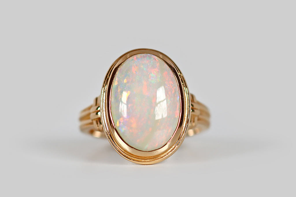 Antique Jewelry Portland, Vintage Jewelry Portland , Antique Engagement Rings | Poor Mouchette | A charming 1940's ring, modeled in 14k rosy yellow gold, whose smooth stepped bezel holds a large, oval, Australian opal cabochon. This opal's soft fire is displayed in the full spectrum of colors, from blue, green, yellow, and pink, to blue and purple. These pastel, rainbow-colored flashes have a linear quality, traveling across the face of the gemstone from north to south.