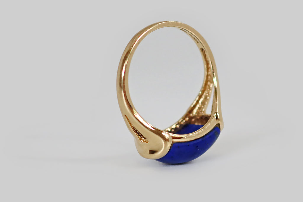 Antique Jewelry Portland, Vintage Jewelry Portland , Antique Engagement Rings | Poor Mouchette | A late vintage saddle ring, modeled in 14k yellow gold, whose gem is a brilliant blue lapis lazuli cabochon. This high-dome, rectangular lapis is beautifully figured with flecks of golden pyrite that splash across its face, on the diagonal. It is set east-to-west in the ring head, where it is mounted in two long tabs that seem to hold it aloft, like a vice.