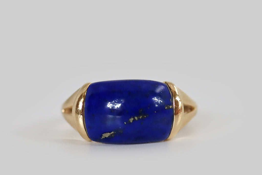 Antique Jewelry Portland, Vintage Jewelry Portland , Antique Engagement Rings | Poor Mouchette | A late vintage saddle ring, modeled in 14k yellow gold, whose gem is a brilliant blue lapis lazuli cabochon. This high-dome, rectangular lapis is beautifully figured with flecks of golden pyrite that splash across its face, on the diagonal. It is set east-to-west in the ring head, where it is mounted in two long tabs that seem to hold it aloft, like a vice.