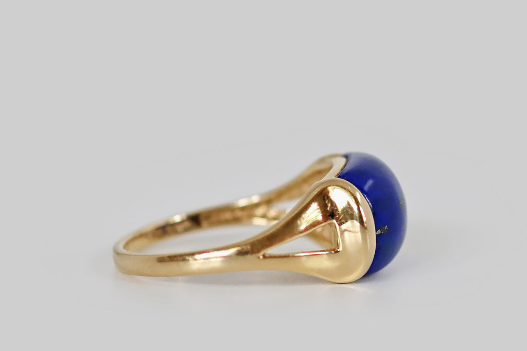 Antique Jewelry Portland, Vintage Jewelry Portland , Antique Engagement Rings | Poor Mouchette | A late vintage saddle ring, modeled in 14k yellow gold, whose gem is a brilliant blue lapis lazuli cabochon. This high-dome, rectangular lapis is beautifully figured with flecks of golden pyrite that splash across its face, on the diagonal. It is set east-to-west in the ring head, where it is mounted in two long tabs that seem to hold it aloft, like a vice.