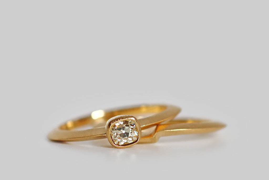Poor Mouchette | Curated Antique Jewelry, Vintage Jewelry & Engagement Rings | Portland, Oregon | A low-profile, solitaire wedding set, modeled in 18k yellow gold, that features an antique .39 carat peruzzi cut diamond (J/VS). This charming antique diamond rests in a smooth bezel that is centered on the ring's dramatic knife-wire shank. The engagement ring is paired with a matching shadow band, that nests with it, perfectly following its lines. This set is both backward and forward looking.