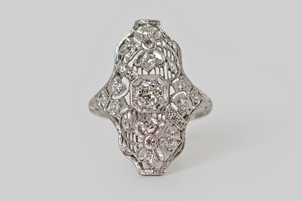 Antique Jewelry Portland, Vintage Jewelry Portland , Antique Engagement Rings | Poor Mouchette | A wonderful Art Deco era shield ring, modeled in platinum, whose artful filigree features four three-leaf clovers resting atop a field of delicate knife wire. The largest of these clovers are stationed to the north and south of the ring's primary diamond, bending gracefully to the right and to the left. This old European cut diamond is mounted in an octagonal seat
