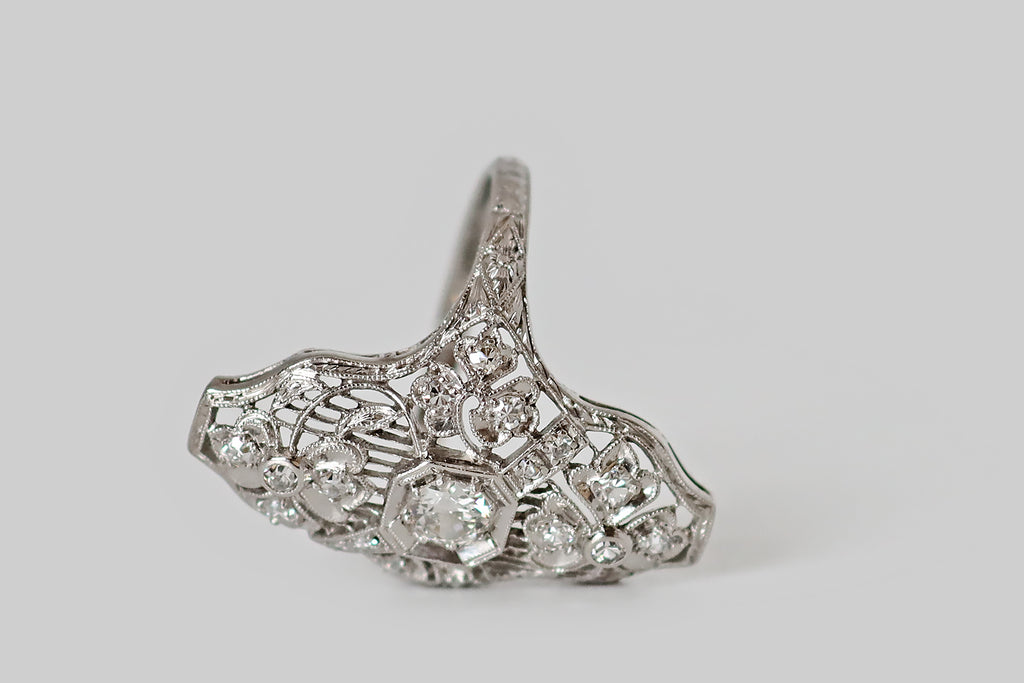 Antique Jewelry Portland, Vintage Jewelry Portland , Antique Engagement Rings | Poor Mouchette | A wonderful Art Deco era shield ring, modeled in platinum, whose artful filigree features four three-leaf clovers resting atop a field of delicate knife wire. The largest of these clovers are stationed to the north and south of the ring's primary diamond, bending gracefully to the right and to the left. This old European cut diamond is mounted in an octagonal seat