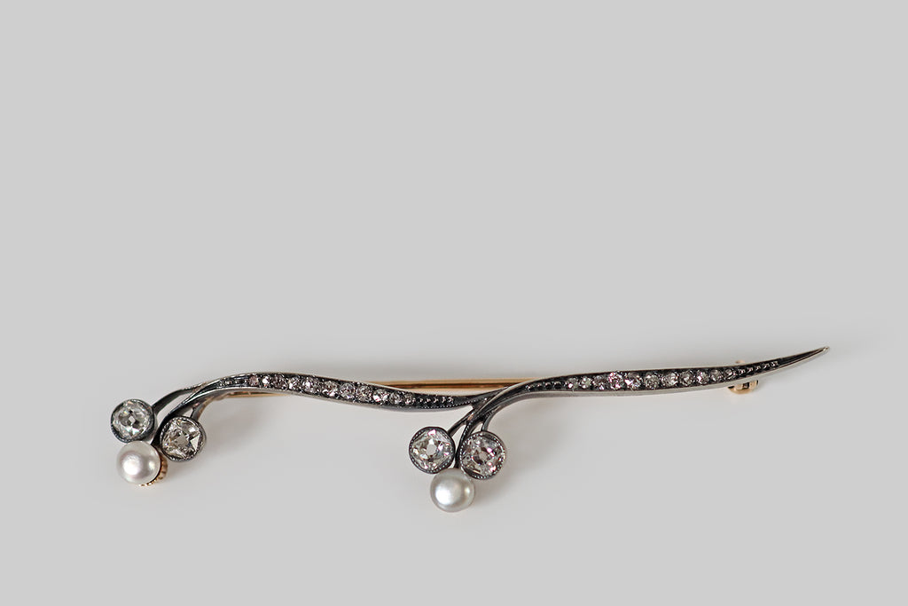Poor Mouchette | Curated Antique Jewelry, Vintage Jewelry & Engagement Rings | Portland, Oregon | An elegant, Art Nouveau era brooch, modeled in rosy 14k yellow gold with a silver top. This antique brooch takes the form of a graceful stem, with two nodding trefoil blossoms. The ribbon-like stems, here, are bead-set with small old mine cut diamonds that graduate toward the center. The trefoil blossoms are each composed of two larger, bezel-set, early old mine cut diamonds