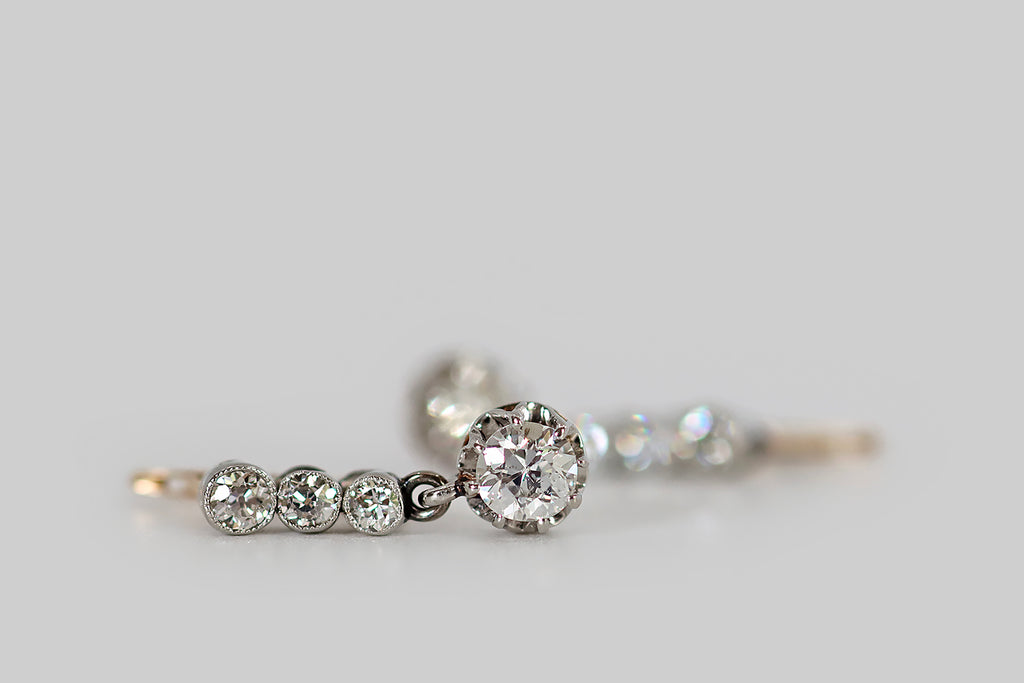 Poor Mouchette | Curated Antique Jewelry, Vintage Jewelry & Engagement Rings | Portland, Oregon | A wonderful pair of Art Deco era earrings, modeled in 14k yellow and white gold, each made-up of a series of three, bezel-set, old mine cute diamonds, and a larger, old European cut diamond drop. Our diamond trios are arranged in vertical lines, where they are held in hand-fabricated, white gold bezels— below this "diamond line
