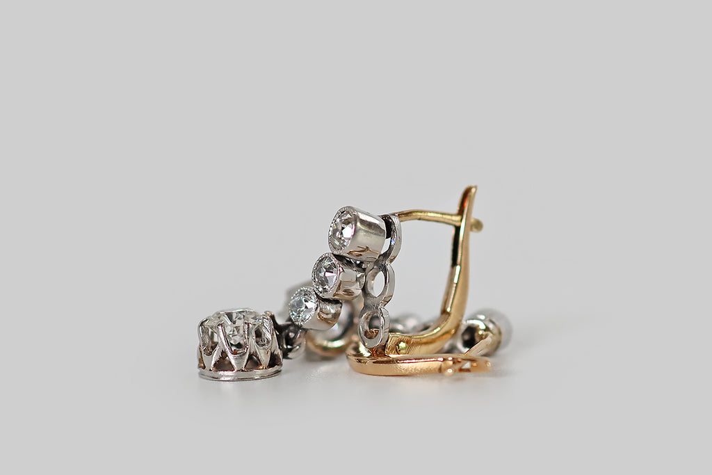 Poor Mouchette | Curated Antique Jewelry, Vintage Jewelry & Engagement Rings | Portland, Oregon | A wonderful pair of Art Deco era earrings, modeled in 14k yellow and white gold, each made-up of a series of three, bezel-set, old mine cute diamonds, and a larger, old European cut diamond drop. Our diamond trios are arranged in vertical lines, where they are held in hand-fabricated, white gold bezels— below this "diamond line