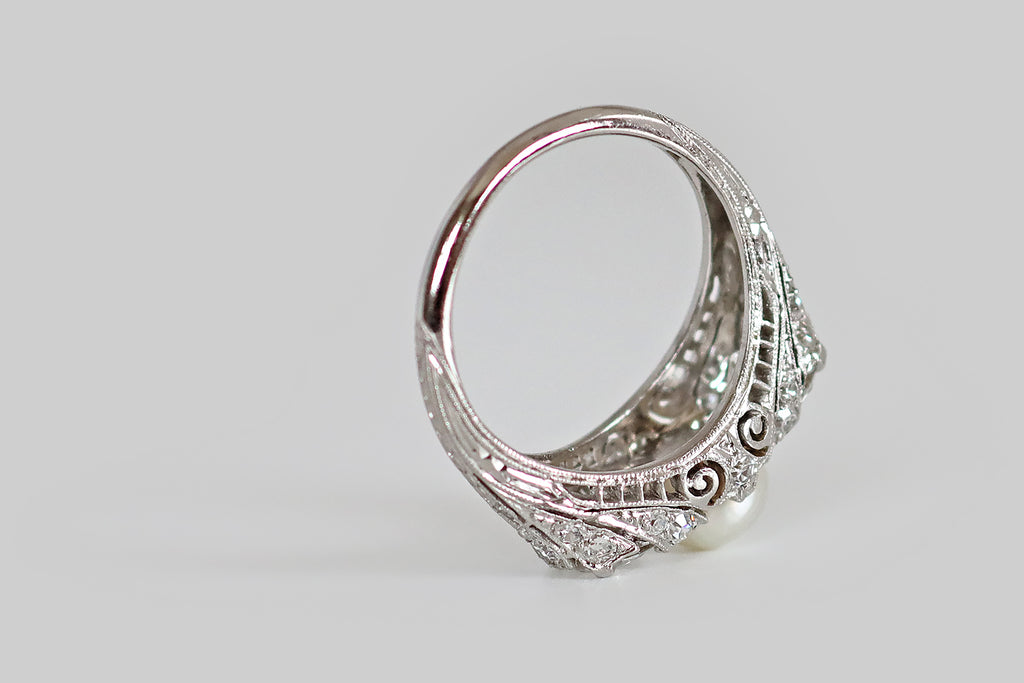 Antique Jewelry Portland, Vintage Jewelry Portland , Antique Engagement Rings | Poor Mouchette | An early 20th century three stone ring, modeled in platinum, whose primary gems are a pair of old European cut diamonds (1.7 carats, together) and a luminous, natural sea pearl. These antique diamonds are held in low-profile, tab-style prongs, where they flank the ring's silvery button pearl. Framing these gems, a wave-like series of diamond-set forms that seem to "splash up" from the ring's gallery and shoulder