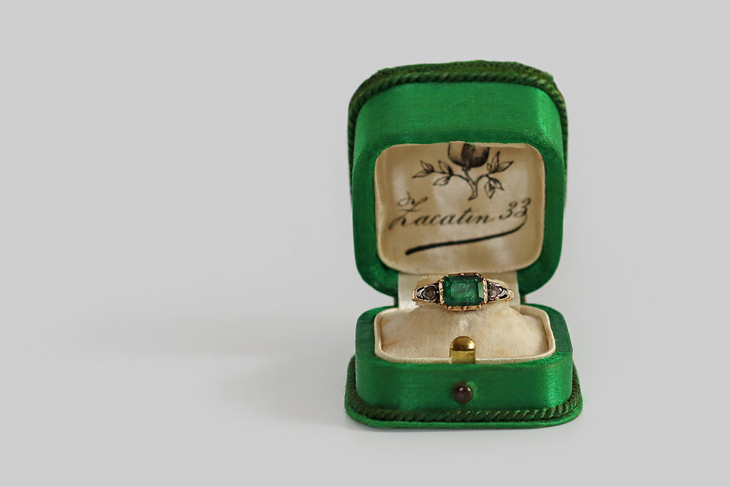 Antique Jewelry Portland, Vintage Jewelry Portland , Antique Engagement Rings | Poor Mouchette |A soulful Georgian-era ring, modeled in 14k gold and silver, whose primary gem is a natural, foiled, emerald cut emerald (approx 1 carat). This vibrant old gem is held in a cut-down collet, where it is flanked by a pair of flinty, rose cut diamonds. The rose cut diamonds nest in silver seats that read like plumes, or trailing folate forms. This ring has a closed back that is beautifully engraved with shell-like 