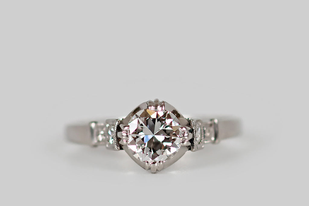 Antique Jewelry Portland, Vintage Jewelry Portland , Antique Engagement Rings | Poor Mouchette | An unusual, Art Moderne era engagement ring, modeled in platinum, whose primary gem is a .62 carat transitional cut diamond (F/G, VS1). This sparkling old cut diamond is held in a modernized buttercup mount, where it is held in four, claw-like, triple prong tabs. Astride this diamond, a pair of accent diamonds rest in square plaques that decorate the ring's cathedral shoulders.