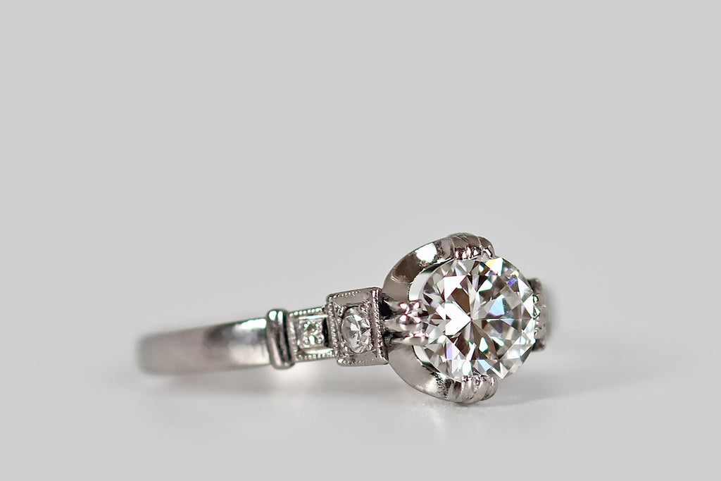 Antique Jewelry Portland, Vintage Jewelry Portland , Antique Engagement Rings | Poor Mouchette | An unusual, Art Moderne era engagement ring, modeled in platinum, whose primary gem is a .62 carat transitional cut diamond (F/G, VS1). This sparkling old cut diamond is held in a modernized buttercup mount, where it is held in four, claw-like, triple prong tabs. Astride this diamond, a pair of accent diamonds rest in square plaques that decorate the ring's cathedral shoulders.