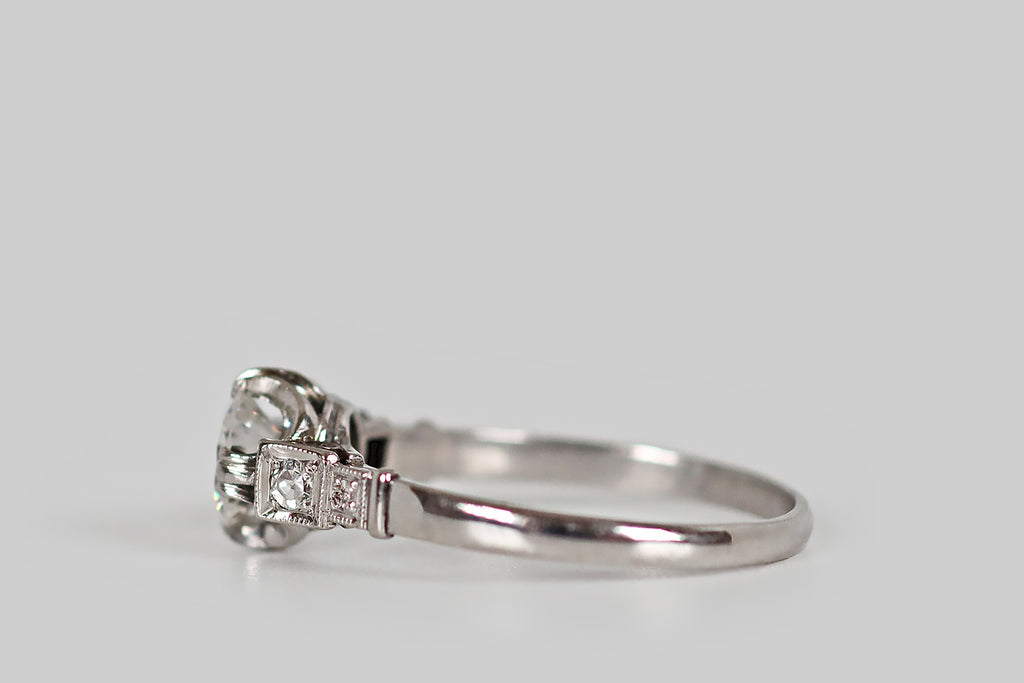 Antique Jewelry Portland, Vintage Jewelry Portland , Antique Engagement Rings | Poor Mouchette | An unusual, Art Moderne era engagement ring, modeled in platinum, whose primary gem is a .62 carat transitional cut diamond (F/G, VS1). This sparkling old cut diamond is held in a modernized buttercup mount, where it is held in four, claw-like, triple prong tabs. Astride this diamond, a pair of accent diamonds rest in square plaques that decorate the ring's cathedral shoulders.