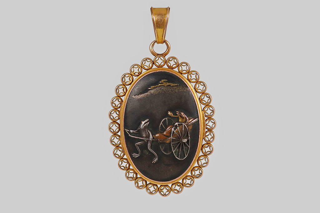 Poor Mouchette | Curated Antique Jewelry, Vintage Jewelry & Engagement Rings | Portland, Oregon | A wonderful, Victorian-era, two-sided locket, whose weighty, hand-fabricated, 14k yellow gold frame is decorated with a repeating, open-work coin motif. This long, oval locket frame holds a pair of shakudo panels— one depicts a pair of frogs in a charming rickshaw scene, the other an Edo-era ship (sengoku-bune) 