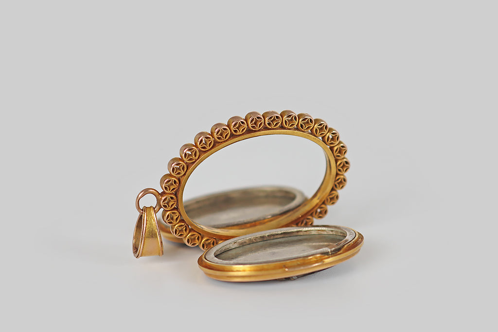 Poor Mouchette | Curated Antique Jewelry, Vintage Jewelry & Engagement Rings | Portland, Oregon | A wonderful, Victorian-era, two-sided locket, whose weighty, hand-fabricated, 14k yellow gold frame is decorated with a repeating, open-work coin motif. This long, oval locket frame holds a pair of shakudo panels— one depicts a pair of frogs in a charming rickshaw scene, the other an Edo-era ship (sengoku-bune) 