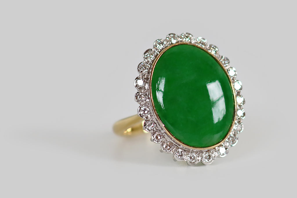 Antique Jewelry Portland, Vintage Jewelry Portland , Antique Engagement Rings | Poor Mouchette | A mid twentieth century cocktail ring, modeled in 14k white and yellow gold, whose primary gem is a large, natural, jadeite jade cabochon. This untreated, 'A jade' cabochon is held in a slim, yellow gold bezel, where it is surrounded by a bevy of sparkling, white, single cut diamonds. This petite diamond border has a charming, scalloped edge