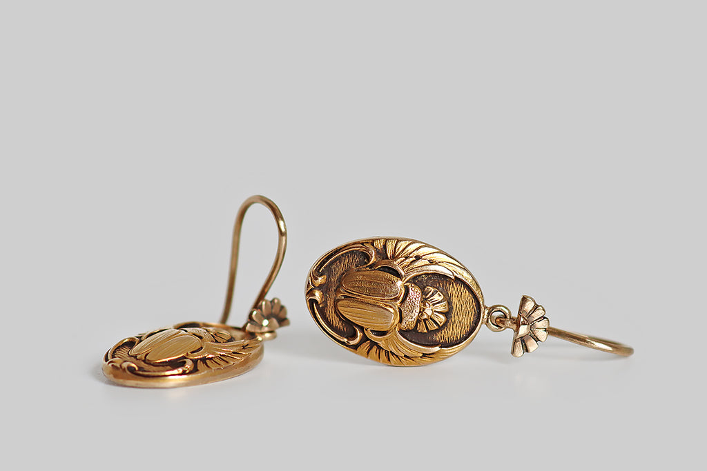 Poor Mouchette | Curated Antique Jewelry, Vintage Jewelry & Engagement Rings | A seriously charming pair of Art Nouveau Egyptian revival earrings, whose oval drops feature a highly detailed and beautifully textured carving of a scarab beetle with open wings. These lovely scarabs hang below a pair of hand-fabricated earwires that are decorated with a motif that repeats the rising sun shape