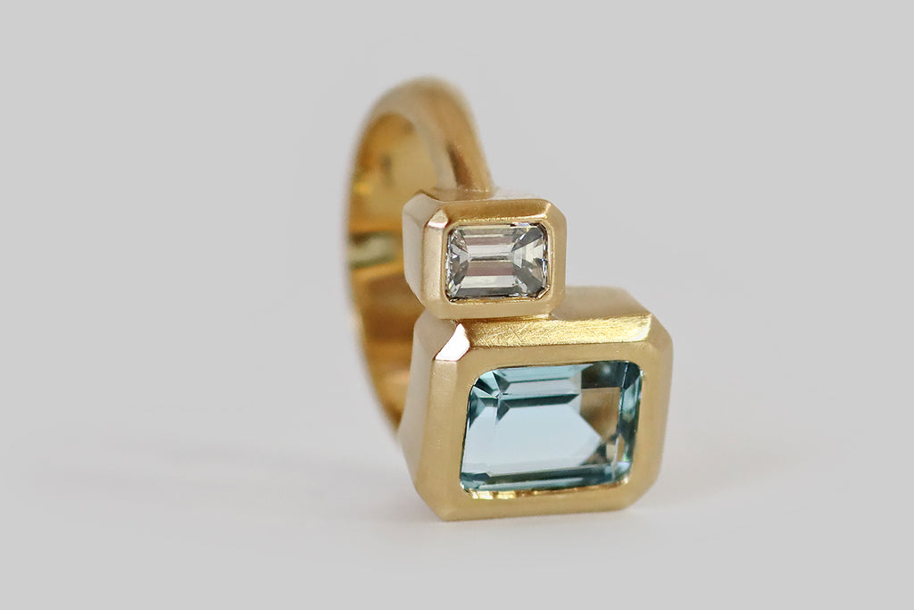 Poor Mouchette | Curated Antique Jewelry, Vintage Jewelry & Engagement Rings | A striking, geometrically-inclined toi et moi ring, modeled in 18k yellow gold, whose gems are a vintage, 2.36 carat emerald cut aquamarine, and vintage emerald cut diamond (G, VS1). These two, elongated gems sit side-by-side (slightly offset) in weighty bezels that trace perfectly the clipped corner facets of our emerald cuts. The ring's half-round shank is very narrow at the shoulder, and it widens like a ribbon toward the base