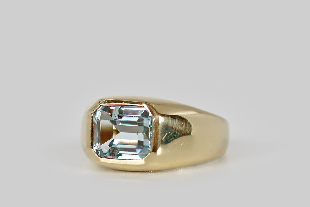 Poor Mouchette | Curated Antique Jewelry, Vintage Jewelry & Engagement Rings | A very cool vintage ring, modeled in 14k yellow gold, whose gem is a large, step-cut aquamarine (about 2.2 carats). This emerald cut aquamarine is held in a burnished, low-profile bezel atop the ring's signet-style head. The ring's integral shank is wide at the shoulder, tapering gradually toward the base.
