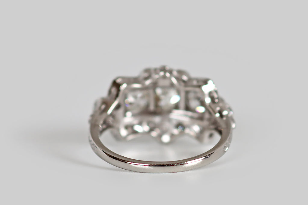 Antique Jewelry Portland, Vintage Jewelry Portland , Antique Engagement Rings | Poor Mouchette | An ornate, Art Deco era, bow-form cluster ring, modeled in platinum, whose primary gems are a trio of sparkling, old European cut diamonds (G/H, VS2-SI1). These three old Euros are arranged horizontally, across the ring face, where they are mounted in square seats and secured with lovely, beaded tabs. Surrounding these three diamonds, the ring's shapely, bow-like form 