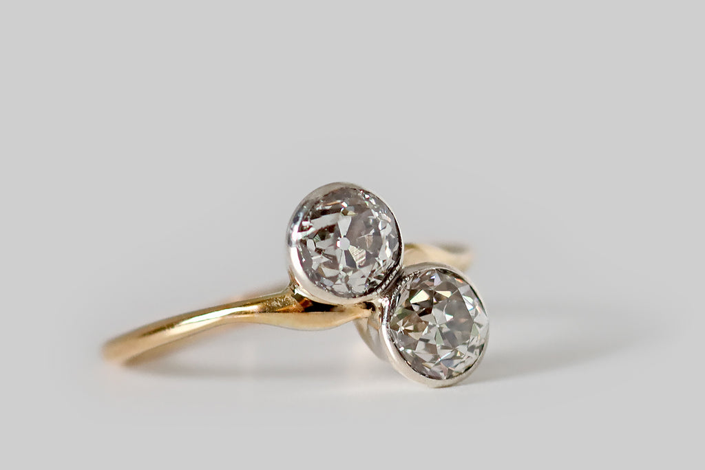 Poor Mouchette | Curated Antique Jewelry, Vintage Jewelry & Engagement Rings | Portland, Oregon | An Art Nouveau era, toi et moi engagement ring, modeled in 14k yellow gold and platinum, whose gems are a pair of soulful, old European cut diamonds (approx 1.25 carats total weight). These OEC diamonds are held in platinum bezels, where they are mounted on the diagonal, atop the ring's curvaceous, whisper-weight shank. Though they are both Old European cuts, the faceting patterns of these two diamonds 