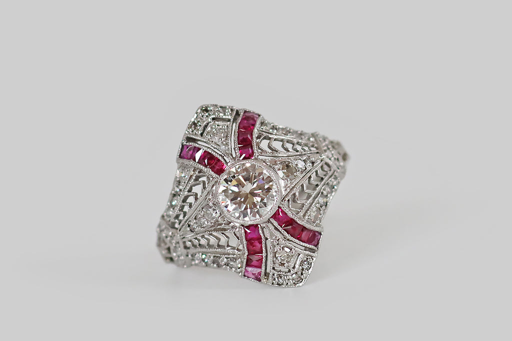 Antique Jewelry Portland, Vintage Jewelry Portland , Antique Engagement Rings | Poor Mouchette | A diamond-shaped, Art Deco era cluster ring, modeled in platinum, whose primary gem is a fiery, half carat transitional cut diamond (G-H, VS1). This soulful old sparkler sits at the center of the ring's face, where it is held in a slim, milgrained bezel. Four sash-like channels curve out from our bezel set diamond, appearing to lay behind it. Astride it, a pair of elongated, diamond-set pennants, framed by lacy 