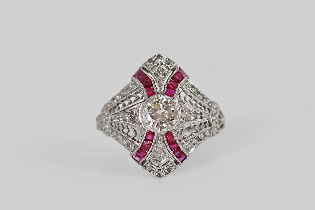Antique Jewelry Portland, Vintage Jewelry Portland , Antique Engagement Rings | Poor Mouchette | A diamond-shaped, Art Deco era cluster ring, modeled in platinum, whose primary gem is a fiery, half carat transitional cut diamond (G-H, VS1). This soulful old sparkler sits at the center of the ring's face, where it is held in a slim, milgrained bezel. Four sash-like channels curve out from our bezel set diamond, appearing to lay behind it. Astride it, a pair of elongated, diamond-set pennants, framed by lacy 