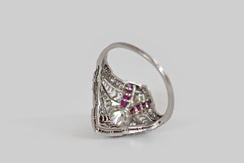 Antique Jewelry Portland, Vintage Jewelry Portland , Antique Engagement Rings | Poor Mouchette | A diamond-shaped, Art Deco era cluster ring, modeled in platinum, whose primary gem is a fiery, half carat transitional cut diamond (G-H, VS1). This soulful old sparkler sits at the center of the ring's face, where it is held in a slim, milgrained bezel. Four sash-like channels curve out from our bezel set diamond, appearing to lay behind it. Astride it, a pair of elongated, diamond-set pennants, framed by lacy 
