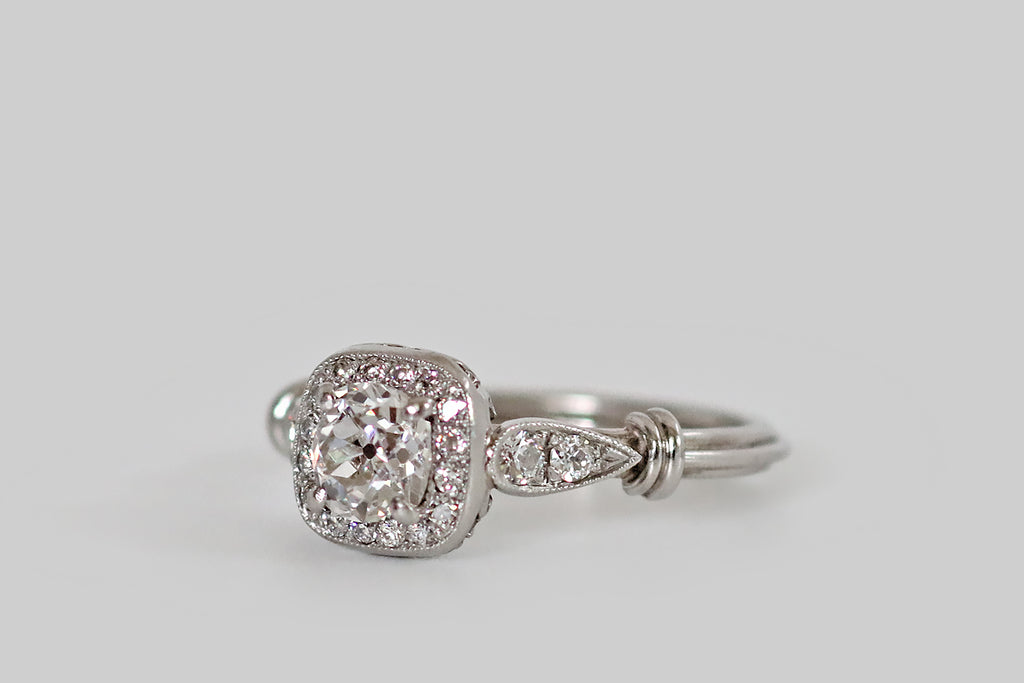 Poor Mouchette | Curated Antique Jewelry, Vintage Jewelry & Engagement Rings | Portland, Oregon | A hand fabricated, Art Deco era cluster ring, modeled in platinum, whose primary gem is a .55 carat old mine cut diamond (G/H, VS2). This soulful, antique diamond is held in four prongs, where it is surrounded by a halo of sixteen smaller old cuts— these supporters are bead set into the ring's cushion-shaped face. This ring features a charming wirework undergallery, and applied, diamond-set, epaulette shoulders