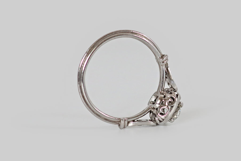 Poor Mouchette | Curated Antique Jewelry, Vintage Jewelry & Engagement Rings | Portland, Oregon | A hand fabricated, Art Deco era cluster ring, modeled in platinum, whose primary gem is a .55 carat old mine cut diamond (G/H, VS2). This soulful, antique diamond is held in four prongs, where it is surrounded by a halo of sixteen smaller old cuts— these supporters are bead set into the ring's cushion-shaped face. This ring features a charming wirework undergallery, and applied, diamond-set, epaulette shoulders