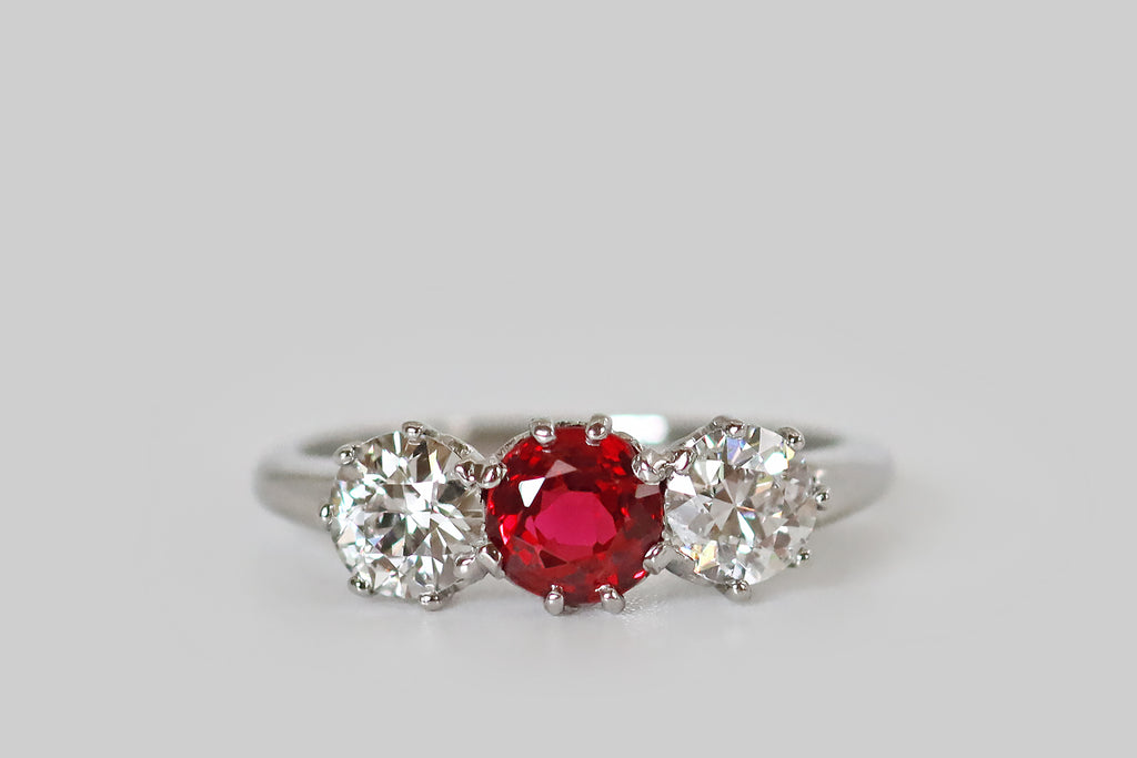 Antique Jewelry Portland, Vintage Jewelry Portland , Antique Engagement Rings | Poor Mouchette | An Art Deco era trilogy ring, fabrictaed in platinum, whose three gemstones are a pair of white, old European cut diamonds, and a natural, vibrant-red spinel. These sparkling gems are arranged horizontally across the ring face, where they are mounted in lacy, eight-prong baskets. The spinel is a rich, bright red color that would rival the best rubies. The diamonds are lively, white and eye clean 