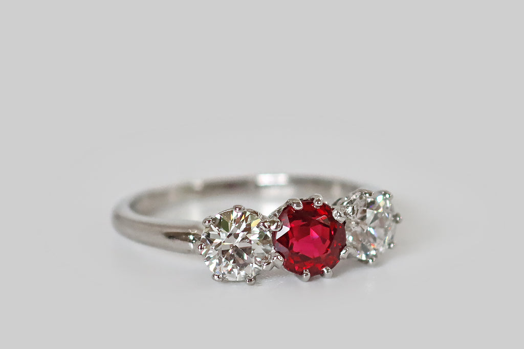 Antique Jewelry Portland, Vintage Jewelry Portland , Antique Engagement Rings | Poor Mouchette | An Art Deco era trilogy ring, fabrictaed in platinum, whose three gemstones are a pair of white, old European cut diamonds, and a natural, vibrant-red spinel. These sparkling gems are arranged horizontally across the ring face, where they are mounted in lacy, eight-prong baskets. The spinel is a rich, bright red color that would rival the best rubies. The diamonds are lively, white and eye clean 
