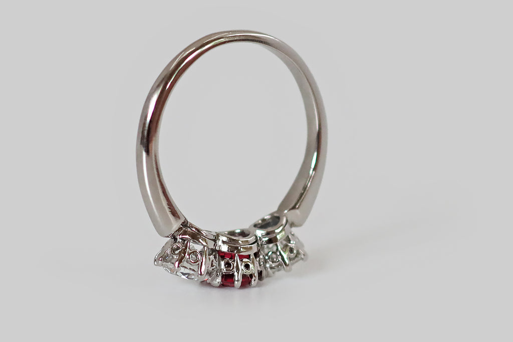 Antique Jewelry Portland, Vintage Jewelry Portland , Antique Engagement Rings | Poor Mouchette | An Art Deco era trilogy ring, fabrictaed in platinum, whose three gemstones are a pair of white, old European cut diamonds, and a natural, vibrant-red spinel. These sparkling gems are arranged horizontally across the ring face, where they are mounted in lacy, eight-prong baskets. The spinel is a rich, bright red color that would rival the best rubies. The diamonds are lively, white and eye clean 