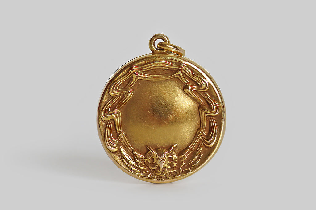 Poor Mouchette | Curated Antique Jewelry, Vintage Jewelry & Engagement Rings | An Art Nouveau era figural locket, modeled in 10k yellow gold, whose decor features an owl with up-stretched wings. This owl motif creates a border around the locket's subtly-domed center. The owl's face sits at the bottom-center of this border, while his feathery wing's ripple out around the locket face, becoming curvaceous, ribbon-like forms that are iconically Art Nouveau.
