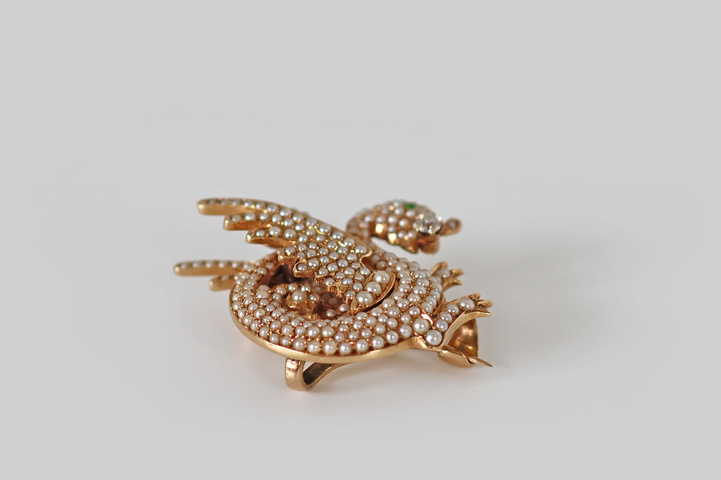 Antique Jewelry Portland, Vintage Jewelry Portland , Antique Engagement Rings | Poor Mouchette |An Art Nouveau era brooch, modeled as an adorable wyvern (dragon) in 14k yellow gold. Our beautiful beast is dimensional, highly stylized, and she is covered with a multitude of tiny natural pearls that represent her scales! She is winged, with two legs, a curling tail, and a vibrant green demantoid garnet eye. She hold an old European cut diamond in her mouth— a treasure that traditionally represents wisdom