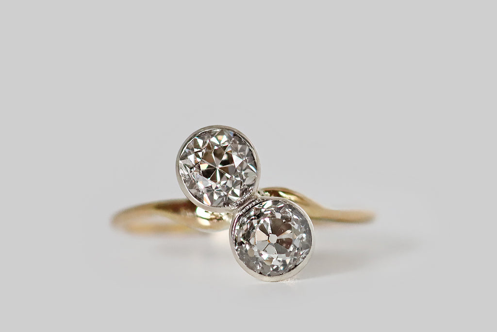 Poor Mouchette | Curated Antique Jewelry, Vintage Jewelry & Engagement Rings | Portland, Oregon | An Art Nouveau era, toi et moi engagement ring, modeled in 14k yellow gold and platinum, whose gems are a pair of soulful, old European cut diamonds (approx 1.25 carats total weight). These OEC diamonds are held in platinum bezels, where they are mounted on the diagonal, atop the ring's curvaceous, whisper-weight shank. Though they are both Old European cuts, the faceting patterns of these two diamonds 