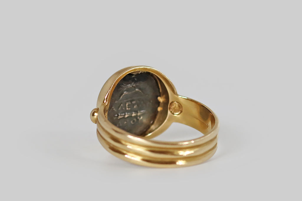 Antique Jewelry Portland, Vintage Jewelry Portland , Antique Engagement Rings | Poor Mouchette | A late-vintage monete style ring, modeled in 14k yellow gold, whose coin features the goddess Athena, wearing a Corinthian helmet. This silver coin is held in a smooth bezel, where it is flanked by a pair of large, granulated beads. The ring's gallery is fashioned with a rolled lip. Its low-profile shank is broad and reeded. Athena is the Greek goddess of wisdom and strategic warfare.