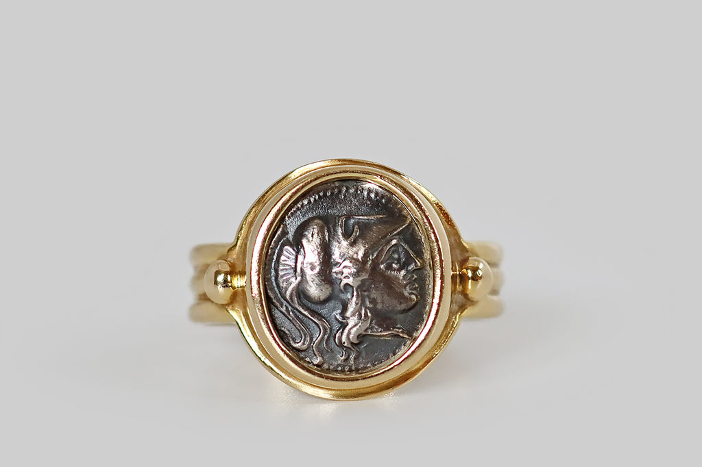 Antique Jewelry Portland, Vintage Jewelry Portland , Antique Engagement Rings | Poor Mouchette | A late-vintage monete style ring, modeled in 14k yellow gold, whose coin features the goddess Athena, wearing a Corinthian helmet. This silver coin is held in a smooth bezel, where it is flanked by a pair of large, granulated beads. The ring's gallery is fashioned with a rolled lip. Its low-profile shank is broad and reeded. Athena is the Greek goddess of wisdom and strategic warfare.