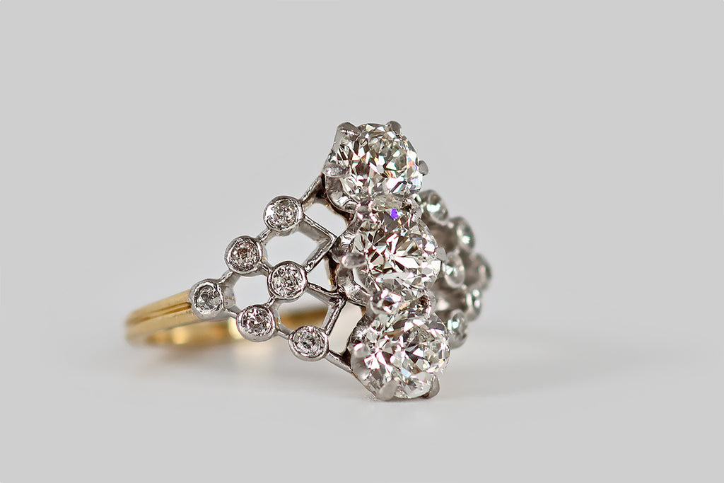 Antique Jewelry Portland, Vintage Jewelry Portland , Antique Engagement Rings | Poor Mouchette | A belle epoque era engagement ring, modeled in 18k yellow gold and platinum, whose face is an openwork, diamond-studded lattice, with three old European cut diamonds resting at center. These primary diamonds (G/H, VS) are arranged in a vertical row, where they are each held in six claw-like prongs. The lattice-work they sit atop is dotted with 12 additional old cut diamonds, that are seated in small