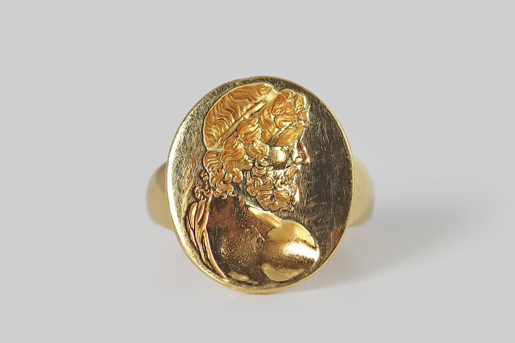 Poor Mouchette | Curated Antique Jewelry, Vintage Jewelry & Engagement Rings | Portland, Oregon | A large vintage signet ring, modeled in 18k yellow gold, whose oval face is decorated with a beautifully-carved, intaglio image of the greek god Zeus. In this rendering, the supreme daddy appears in profile, looking wistful and sensual. His beard is full and wavy; his hair falls in ringlets, below a fillet band. We view him from over a muscular shoulder, as if he were about to turn back